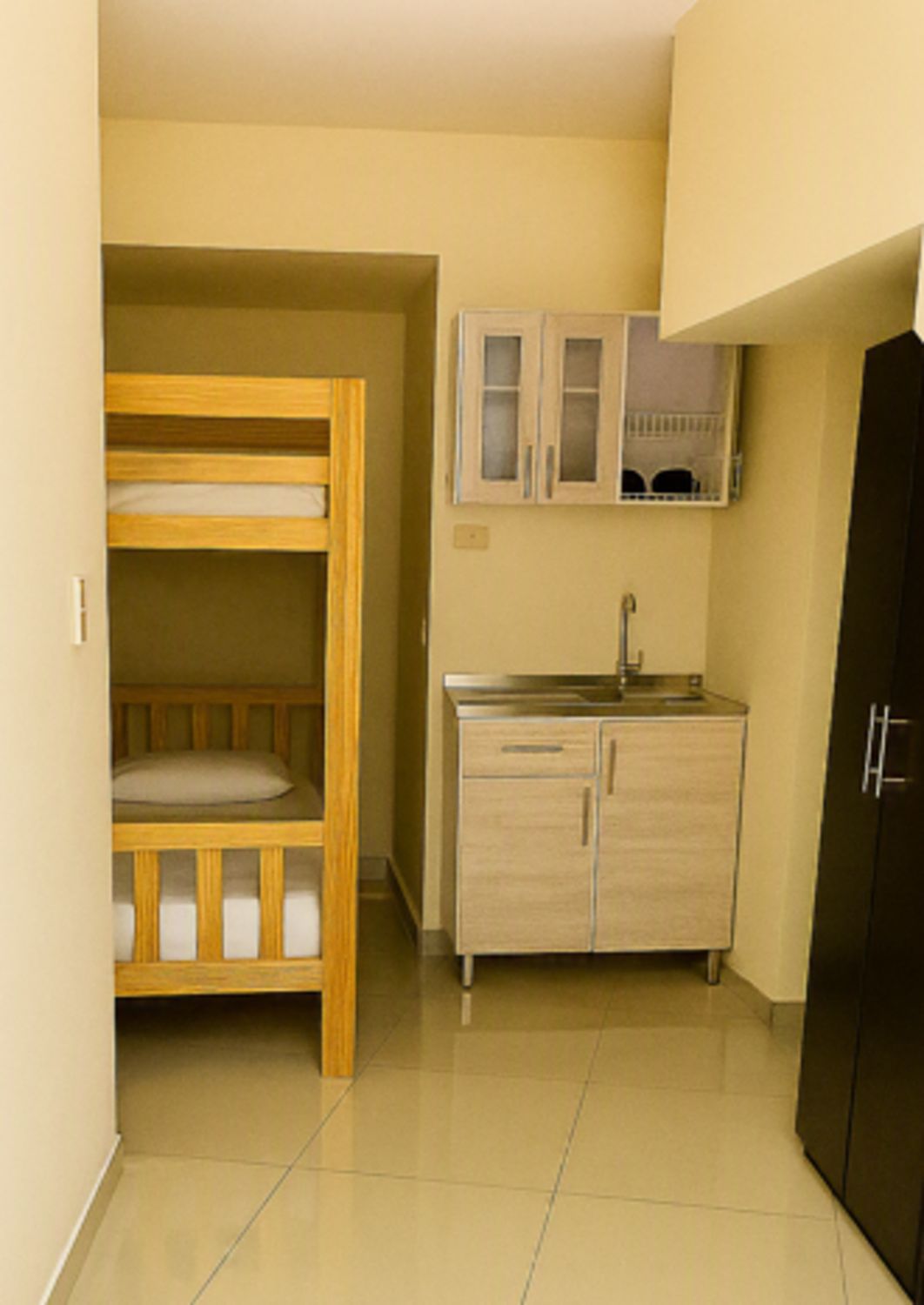 A compact room with a bunk bed, a kitchenette, and a black wardrobe.