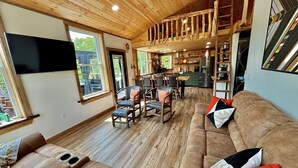 A spacious living area with a wooden ceiling, a large sofa, and a dining area with chairs. - Lakefront, hot tub, 2 bdrm w/ loft, kayaks, beach, fire pits,! sxs trails (La Follette)