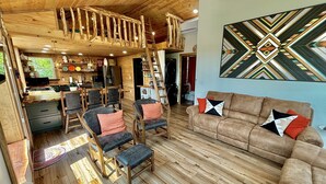 A rustic cabin interior with a wooden floor, a loft bedroom with a wooden railing, and a dining area with a kitchen. - Lakefront, hot tub, 2 bdrm w/ loft, kayaks, beach, fire pits,! sxs trails (La Follette)