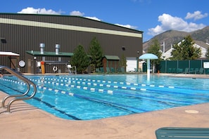 Ein Schwimmbecken mit Bahnen, einem Rettungsschwimmerstand und einem überdachten Sitzbereich.