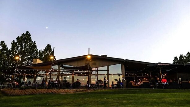 An outdoor venue with a covered seating area, a stage, and a building with large windows.