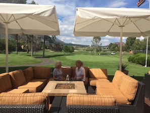 Ein Außenbereich mit gepolsterten Sofas und einem Tisch, umgeben von weißen Sonnenschirmen, mit Blick auf einen Golfplatz.