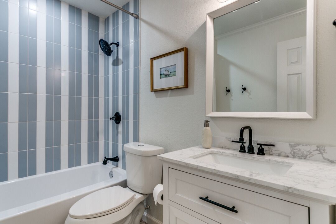 Een badkamer met een badkuip, toilet en wastafel, met streepjestegels en een ingelijst beeld aan de muur.