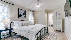 A bedroom with a bed, nightstands, a ceiling fan, a large window, and a dresser. - The Main Street Cottage: Dog-Friendly, Central DFW location, Walk to Main St (Lewisville)