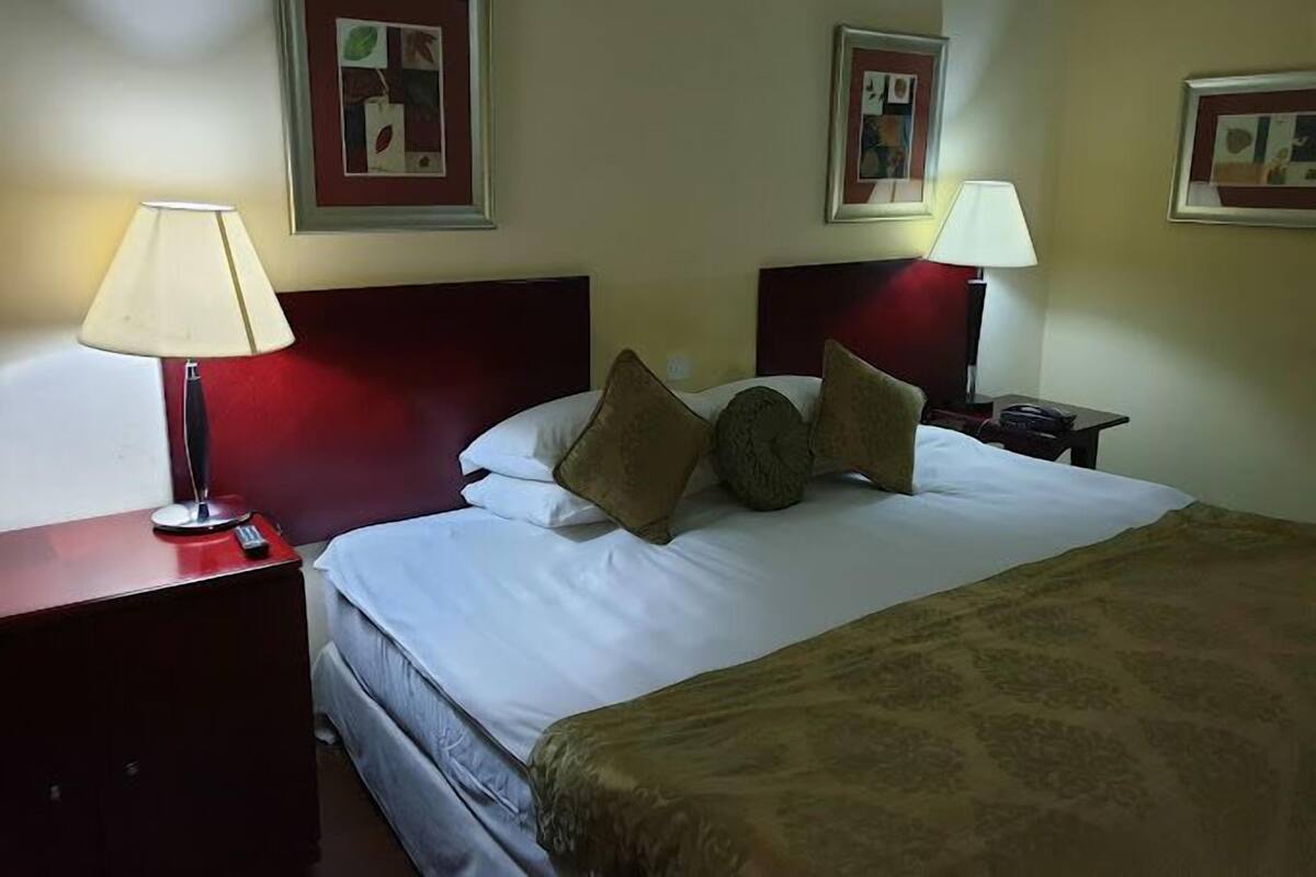 Une chambre d’hôtel avec un lit, deux tables de chevet avec des lampes et des tableaux encadrés aux murs.