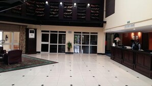 Een ruime lobby met een hoge plafond, een receptiebalie en een groot raam.