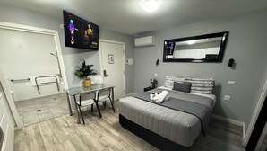 A modern hotel room with a bed, bedside table, and a TV mounted on the wall displaying a movie. - Studio with Disability Access (Adamstown)