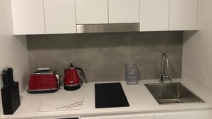 A kitchen with white cabinets, a stainless steel sink, a red toaster, a kettle, and a black cutting board. - Studio with Disability Access (Adamstown)
