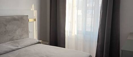 Un dormitorio moderno con una cama, una mesita de noche, una lámpara colgante y una ventana con cortinas.