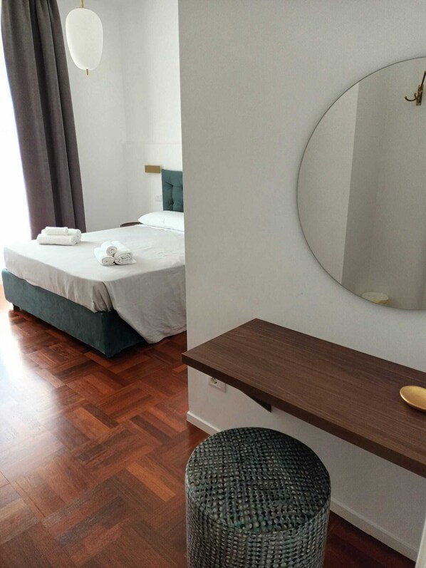 A bedroom with a bed, a bedside table, a round mirror, a small round stool, and a dark wooden floor. - B&Bari via Crollalanza (Bari)
