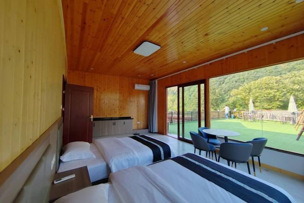 Une chambre avec deux lits, une petite table et une vue sur un jardin.