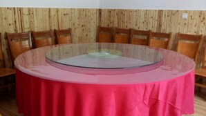 Una mesa redonda de vidrio con mantel rosa, rodeada de sillas de madera.