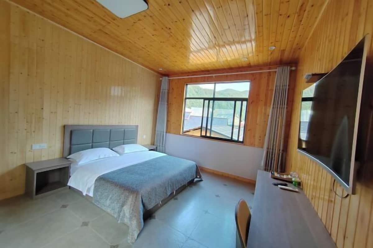 Une pièce aux murs lambrissés, contenant un lit, un bureau, une chaise et un téléviseur.