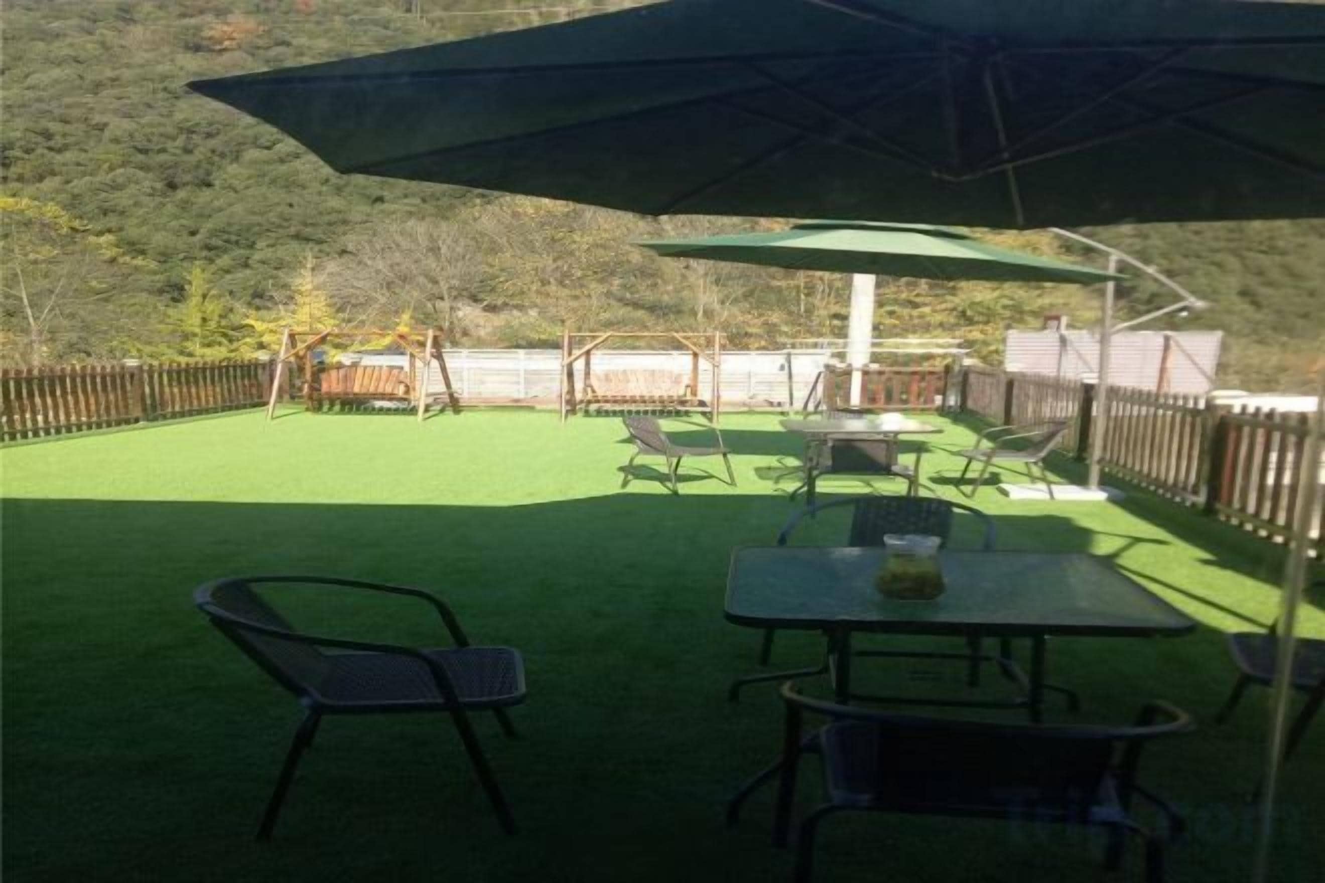 Eine Außenpatio mit Tisch und Stühlen, einem grünen Sonnenschirm und Blick auf eine hügelige Landschaft.