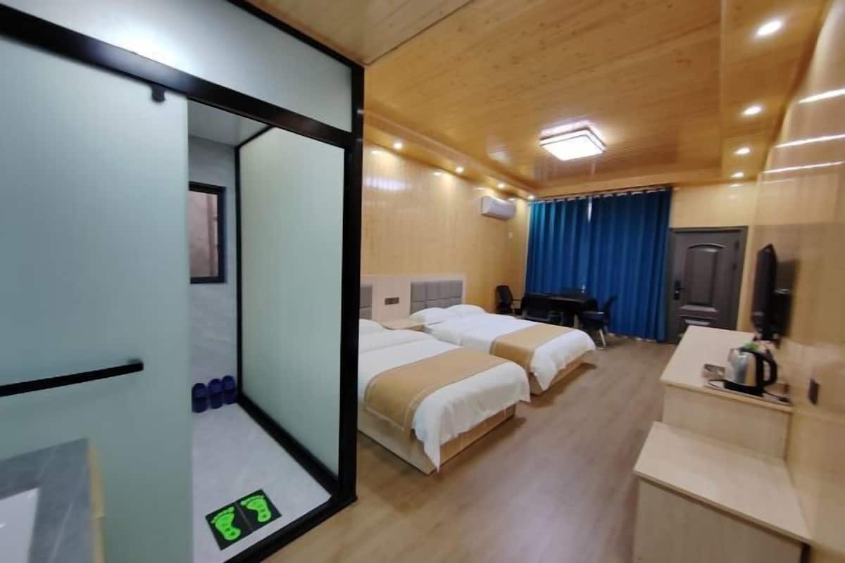 Une chambre d’hôtel avec deux lits, un bureau, une chaise, une télévision et une salle de bain équipée d’un miroir et d’une douche.