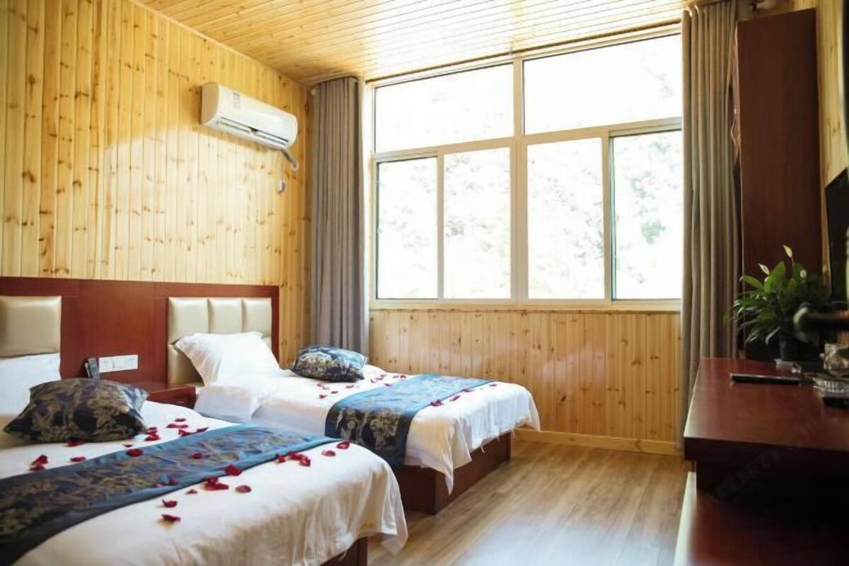 Une chambre avec deux lits, des murs en bois, une grande fenêtre et un appareil de climatisation.
