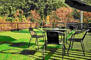 Un patio al aire libre con mesas y sillas, rodeado por una valla de madera y árboles.