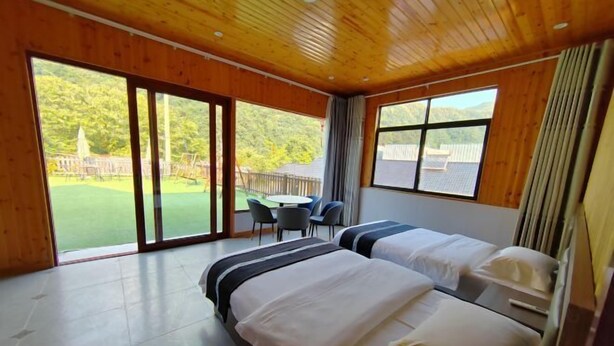 Habitación de hotel con dos camas, un amplio ventanal corredero a un patio con mesa y sillas, y vistas a un paisaje verde.