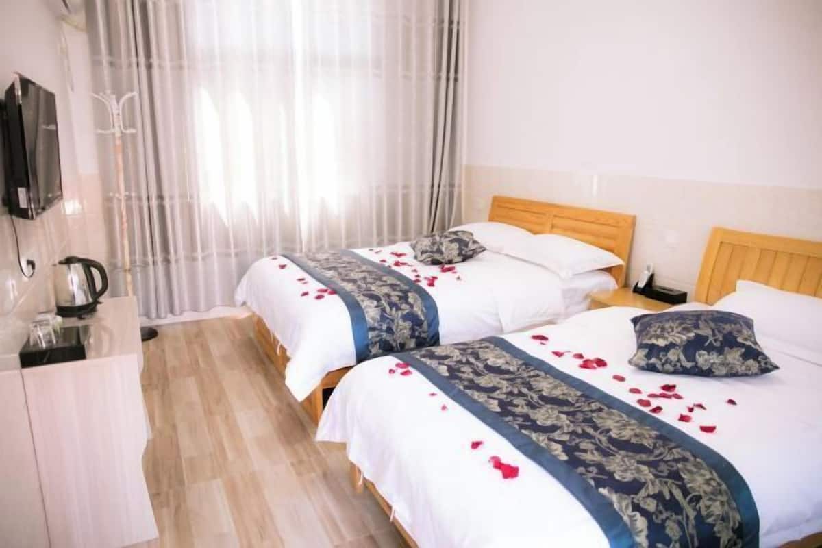 Une chambre d’hôtel avec deux lits, une tête de lit en bois, une table de chevet et un téléviseur fixé au mur.