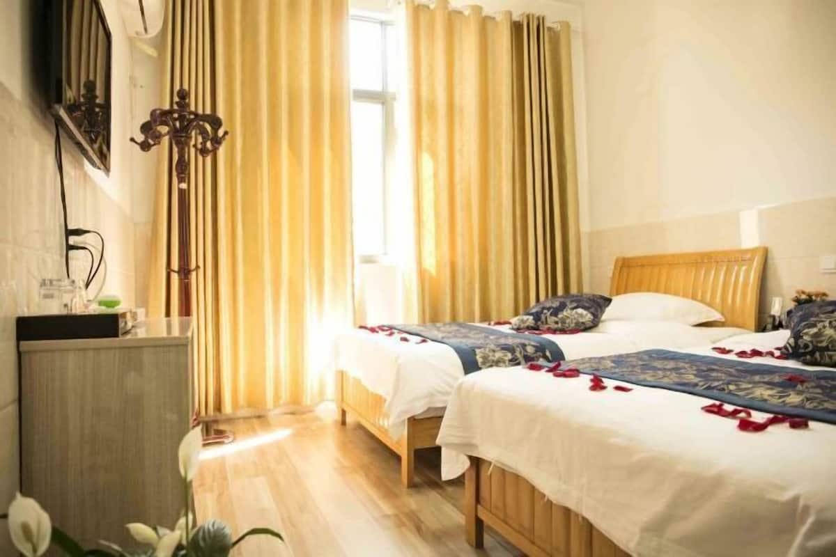 Une chambre d’hôtel avec deux lits, une tête de lit en bois, une table de chevet et une fenêtre avec des rideaux.