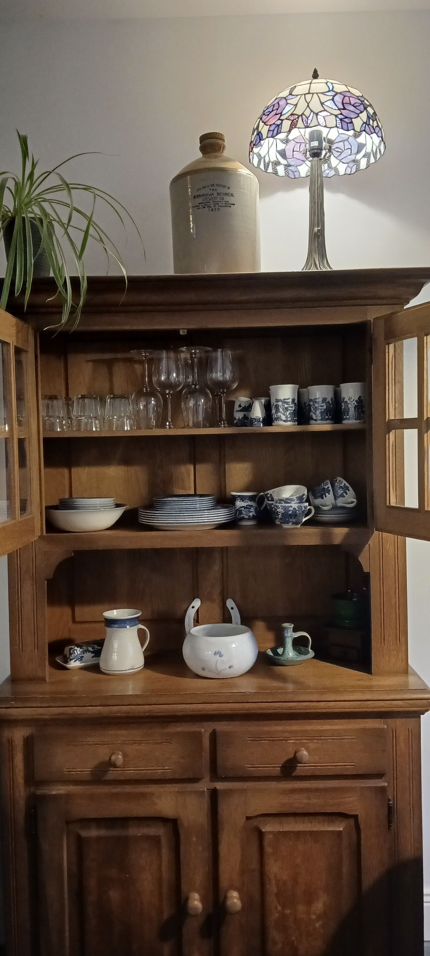 Ein Holzschrank mit Regalen, auf denen verschiedene Gläser, Teller und Tassen stehen.