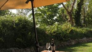 Une table de pique-nique en bois, un grand parasol, une bouteille et un verre de vin.