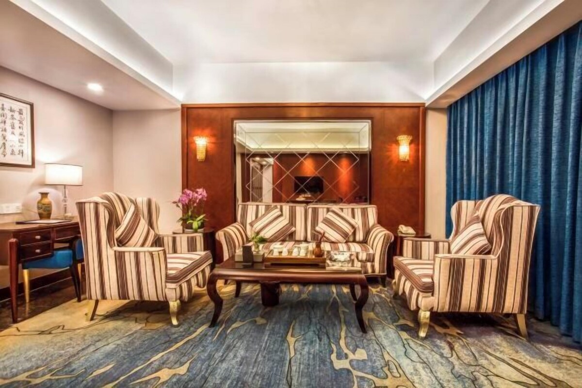A hotel room with a sofa set, a coffee table, a desk with a lamp, and a large mirror.