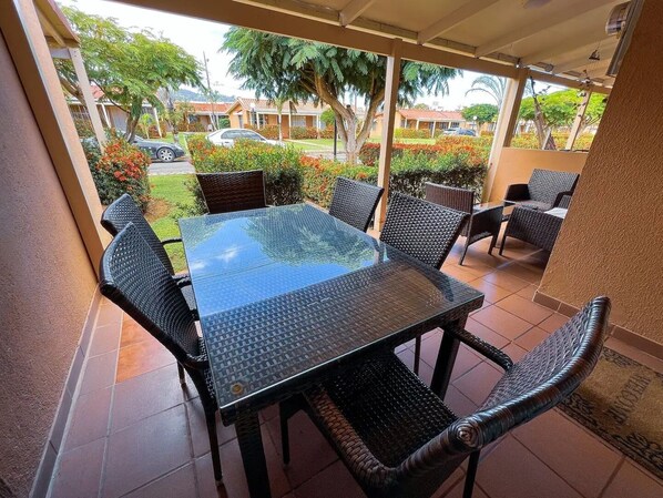 A covered outdoor patio with a glass-top table and wicker chairs. - Villa C20 (Jacó)