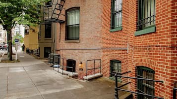 A narrow urban street with red brick buildings, a fire escape, and a sidewalk.