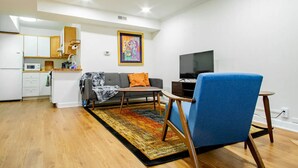 A modern living room with a sofa, a blue armchair, a coffee table, a TV, and a kitchen area with cabinets and a microwave. - A Classy Corner of DC near Dupont Circle (Washington)