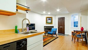 A modern kitchen with a dishwasher, a sink, and a wooden countertop. There is a dining area with a blue chair and a red vase. A television is mounted on the wall, and a painting is visible. - A Classy Corner of DC near Dupont Circle (Washington)