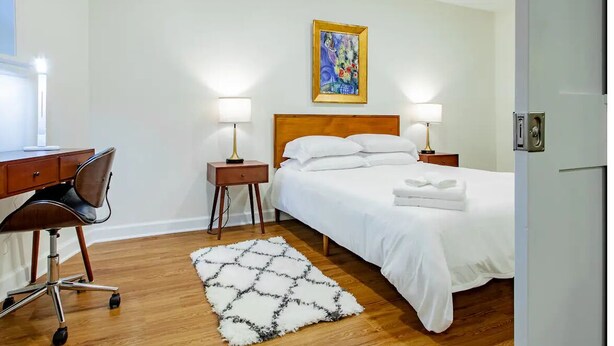 A hotel room with a wooden bed, two bedside lamps, a desk with a chair, and a painting on the wall. - A Classy Corner of DC near Dupont Circle (Washington)