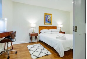 A hotel room with a wooden bed, two bedside lamps, a desk with a chair, and a painting on the wall. - A Classy Corner of DC near Dupont Circle (Washington)