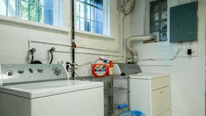 A laundry room with a washing machine, a dryer, and a utility cabinet. There are cleaning supplies on the counter, and a window provides natural light. - A Classy Corner of DC near Dupont Circle (Washington)
