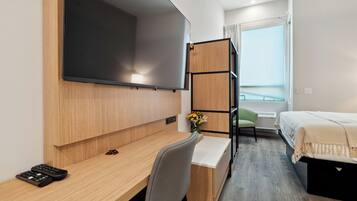A hotel room with a wooden desk, a bed, a TV mounted on the wall, and a window with a view.