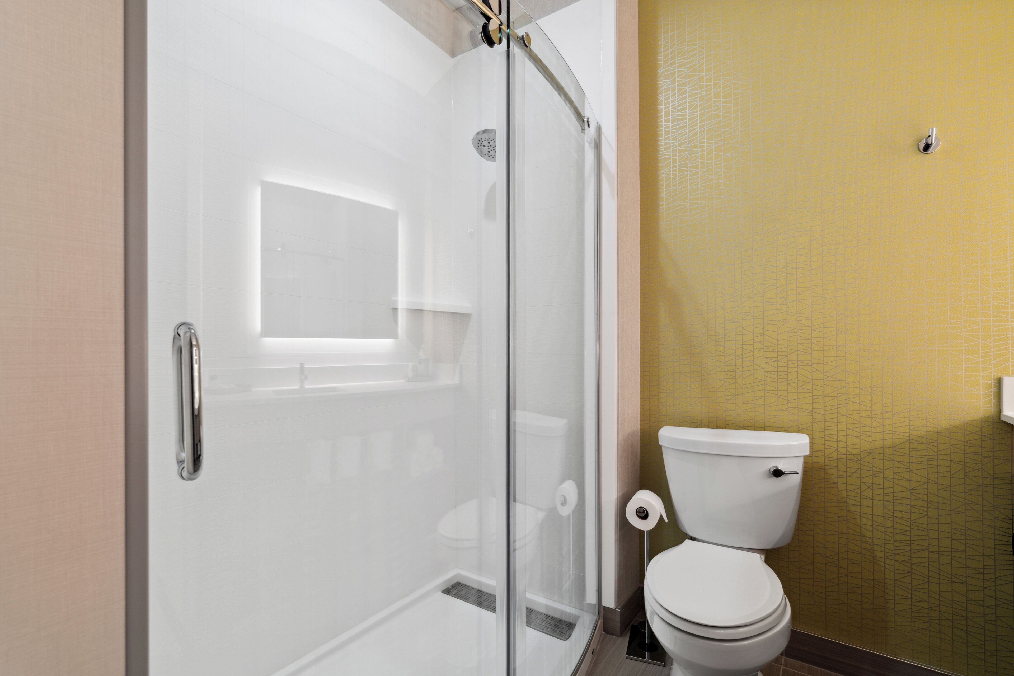 Een badkamer met een douchecabine van glas, een wit toilet en een geel betegelde muur.