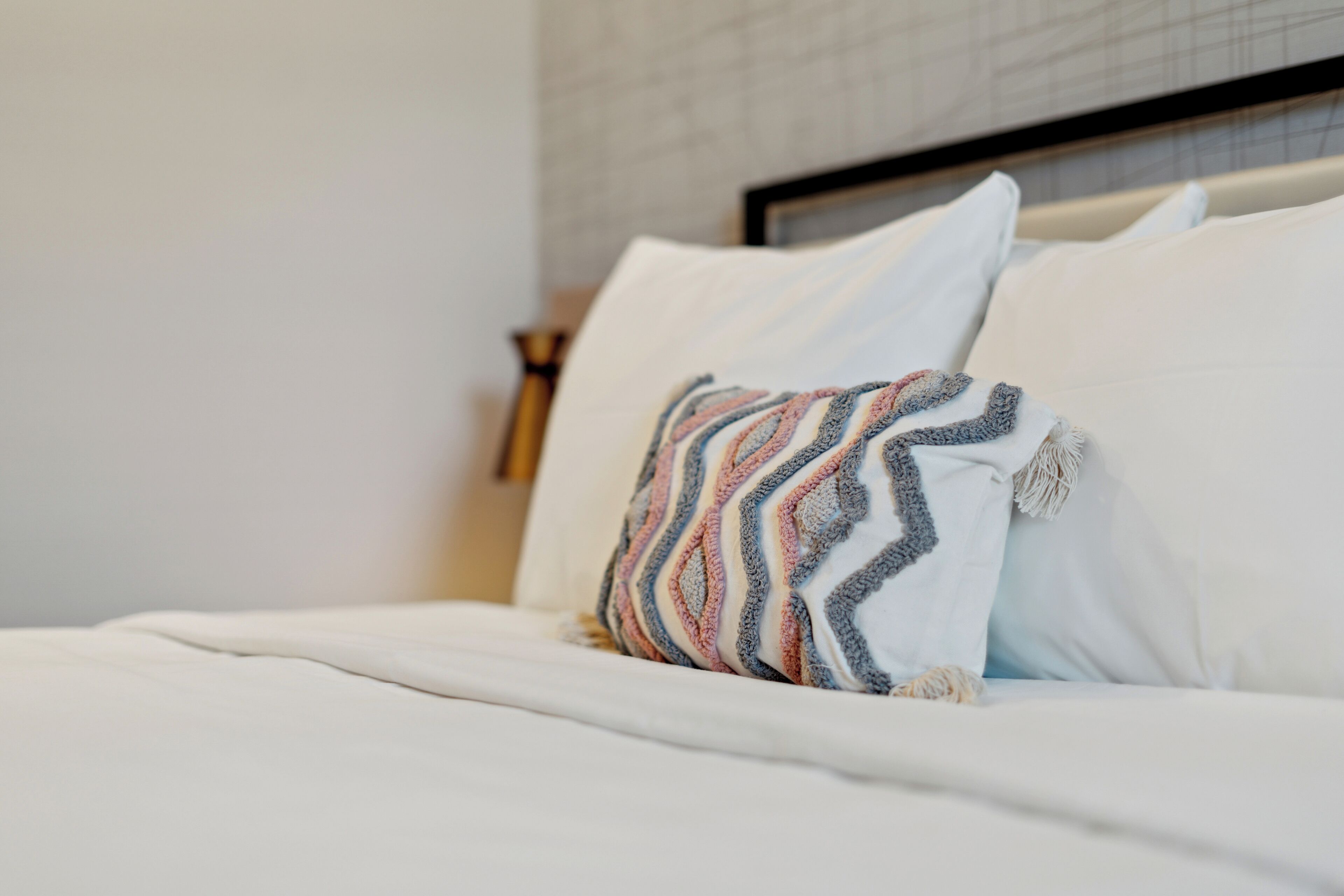 Una cama bien tendida con ropa blanca y un cojín decorativo de estampado en zigzag.