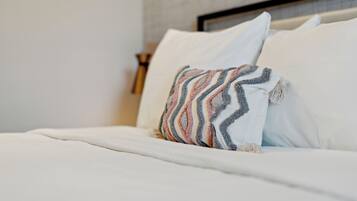 Una cama bien tendida con ropa blanca y un cojín decorativo de estampado en zigzag.