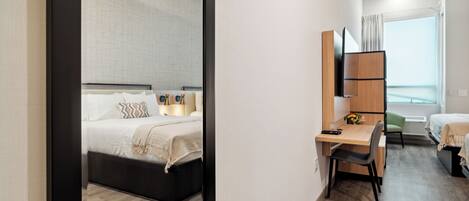 Una habitación de hotel moderna con cama, escritorio, silla y un amplio ventanal con cortinas.