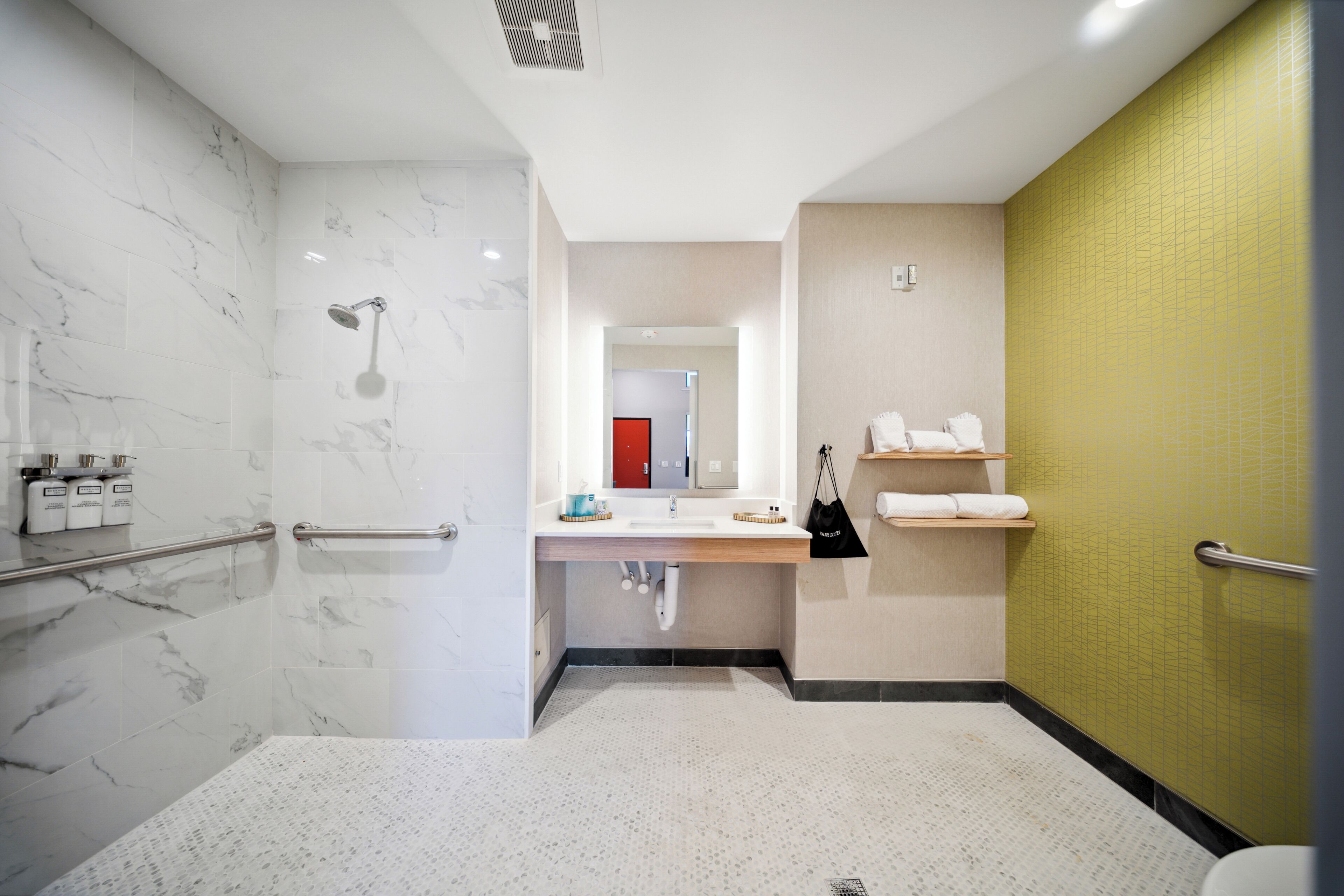 Uma casa de banho moderna com chuveiro de mármore, lavatório com espelho e parede revestida a mosaicos amarelos.
