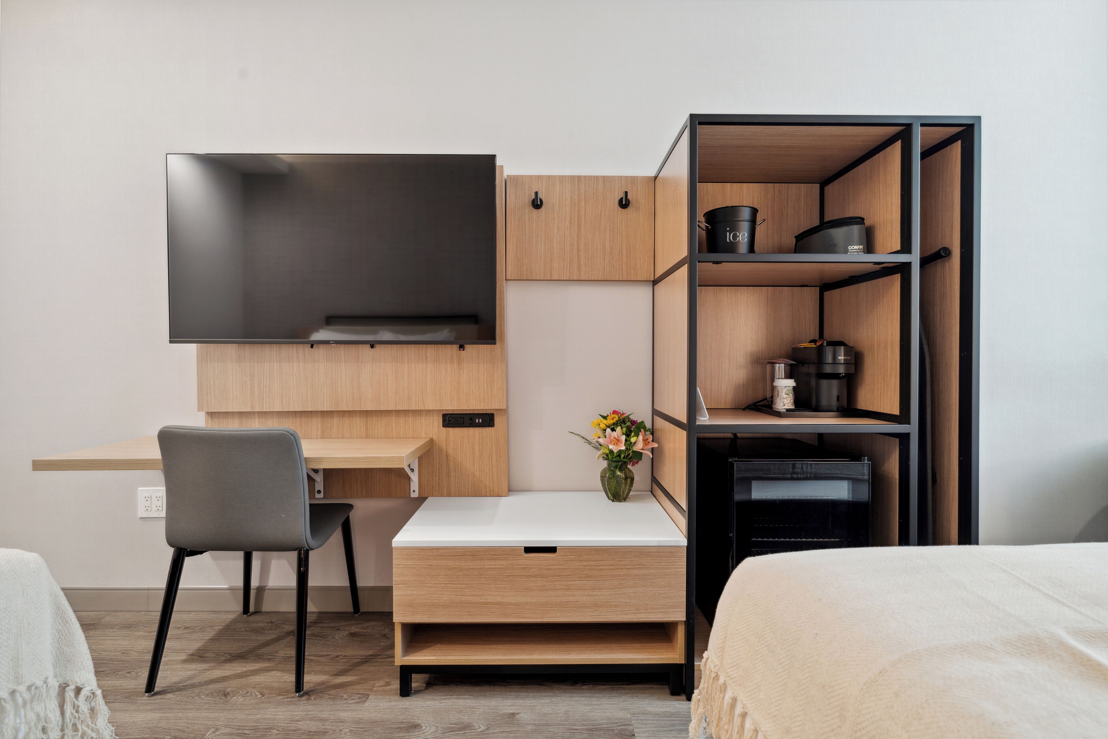 A compact hotel room with a bed, a desk with a chair, a TV, and a kitchenette with cabinets and a microwave.