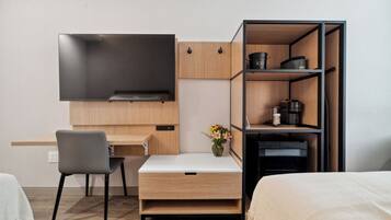 A compact hotel room with a bed, a desk with a chair, a TV, and a kitchenette with cabinets and a microwave.