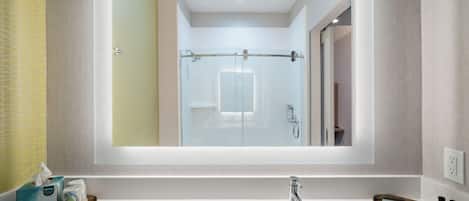 A modern bathroom with a large mirror, a white sink, and a glass shower enclosure.