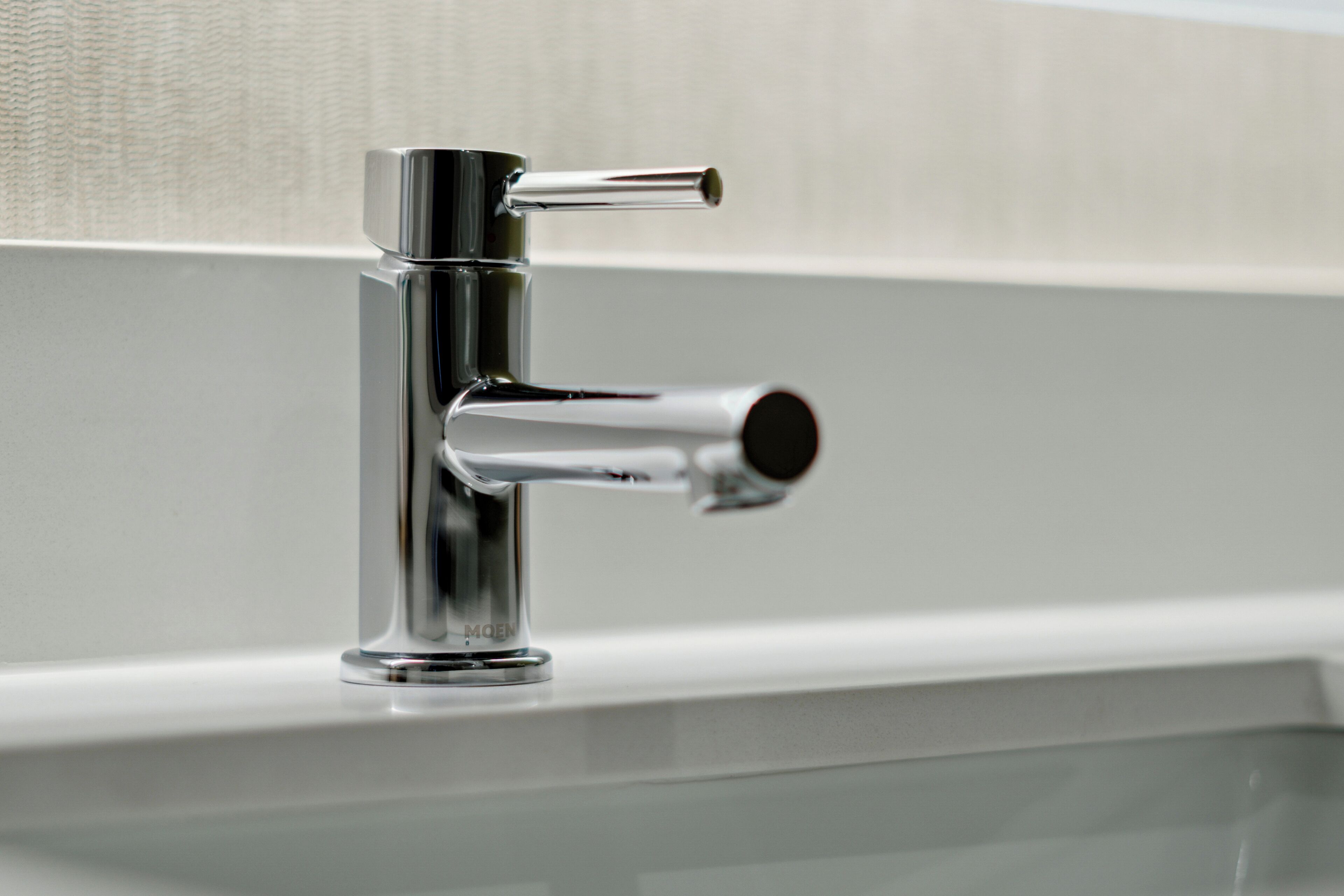 A chrome faucet with a single handle and a spout, mounted on a white wall.