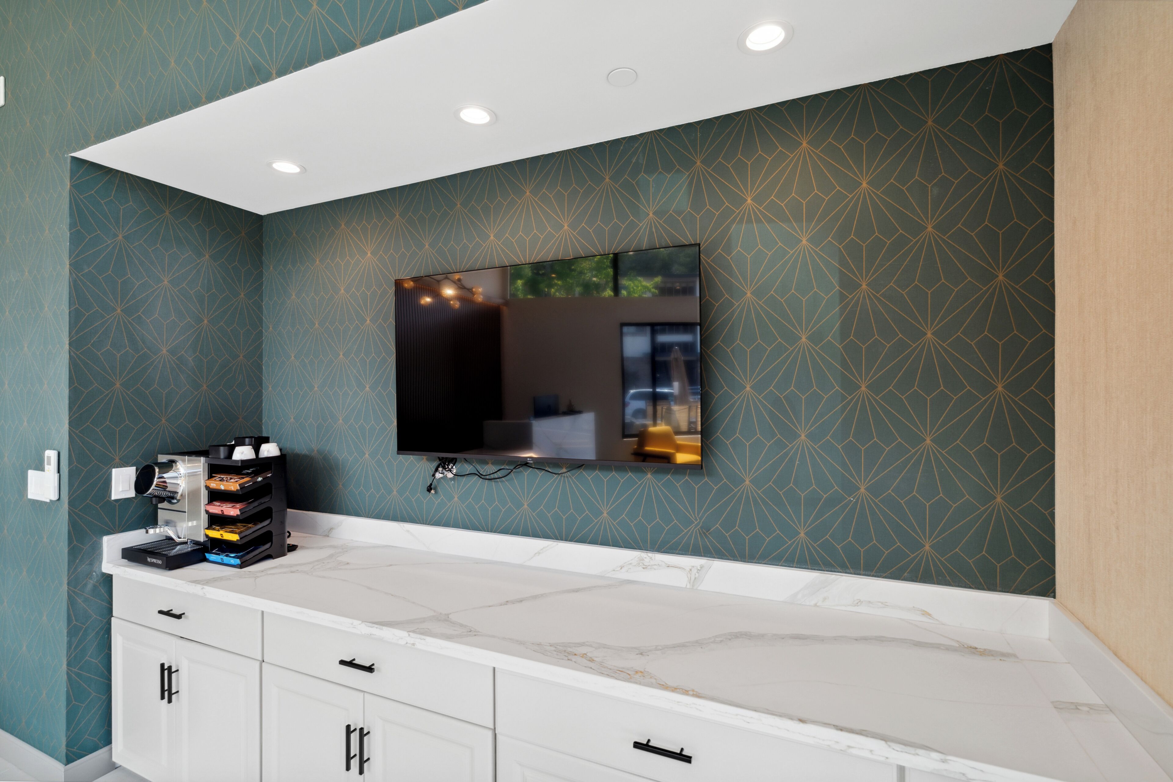 A modern bathroom with a large mirror, a flat-screen TV, and a marble countertop.