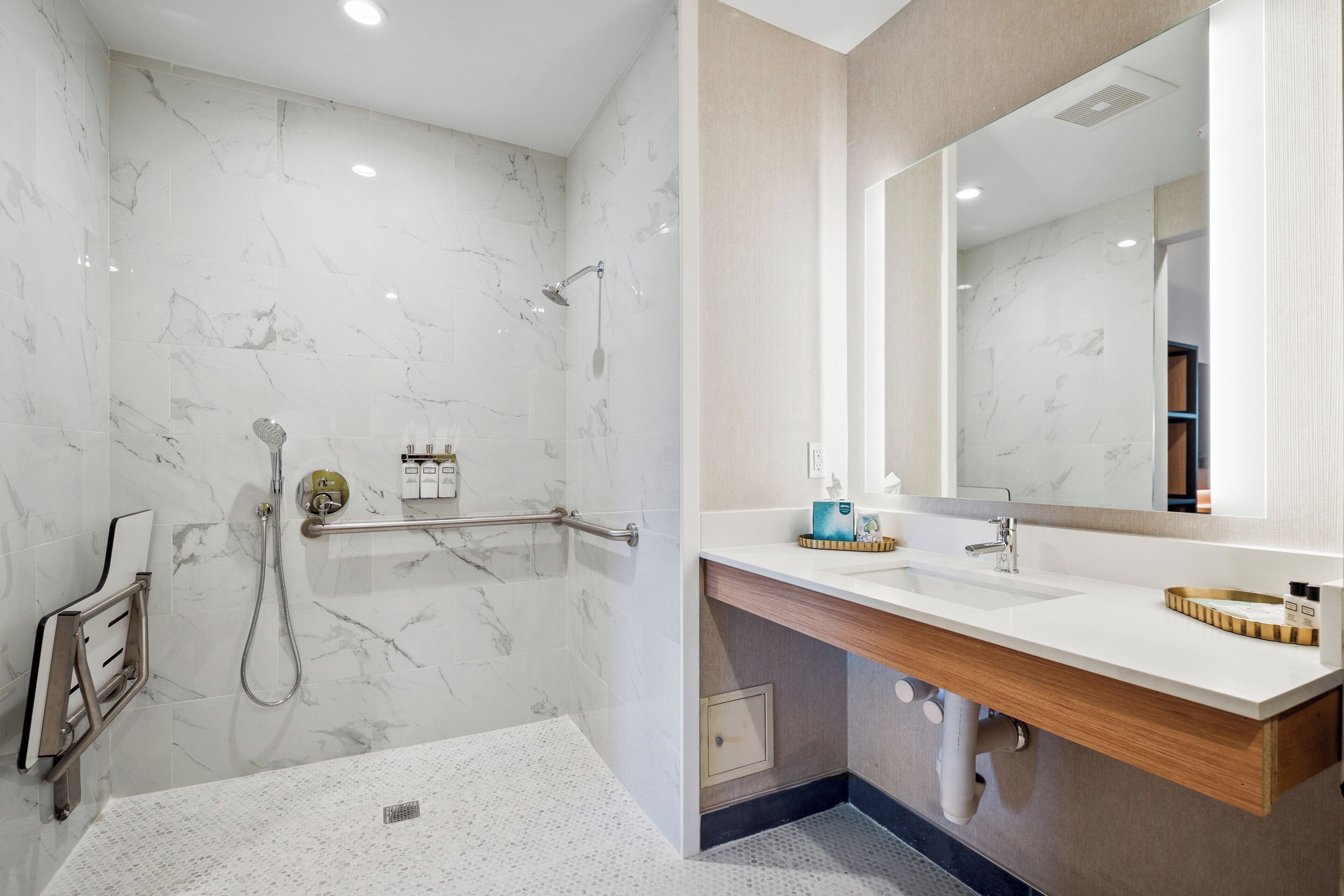 Un baño moderno con ducha de mármol, lavabo con tocador de madera y un espejo grande.