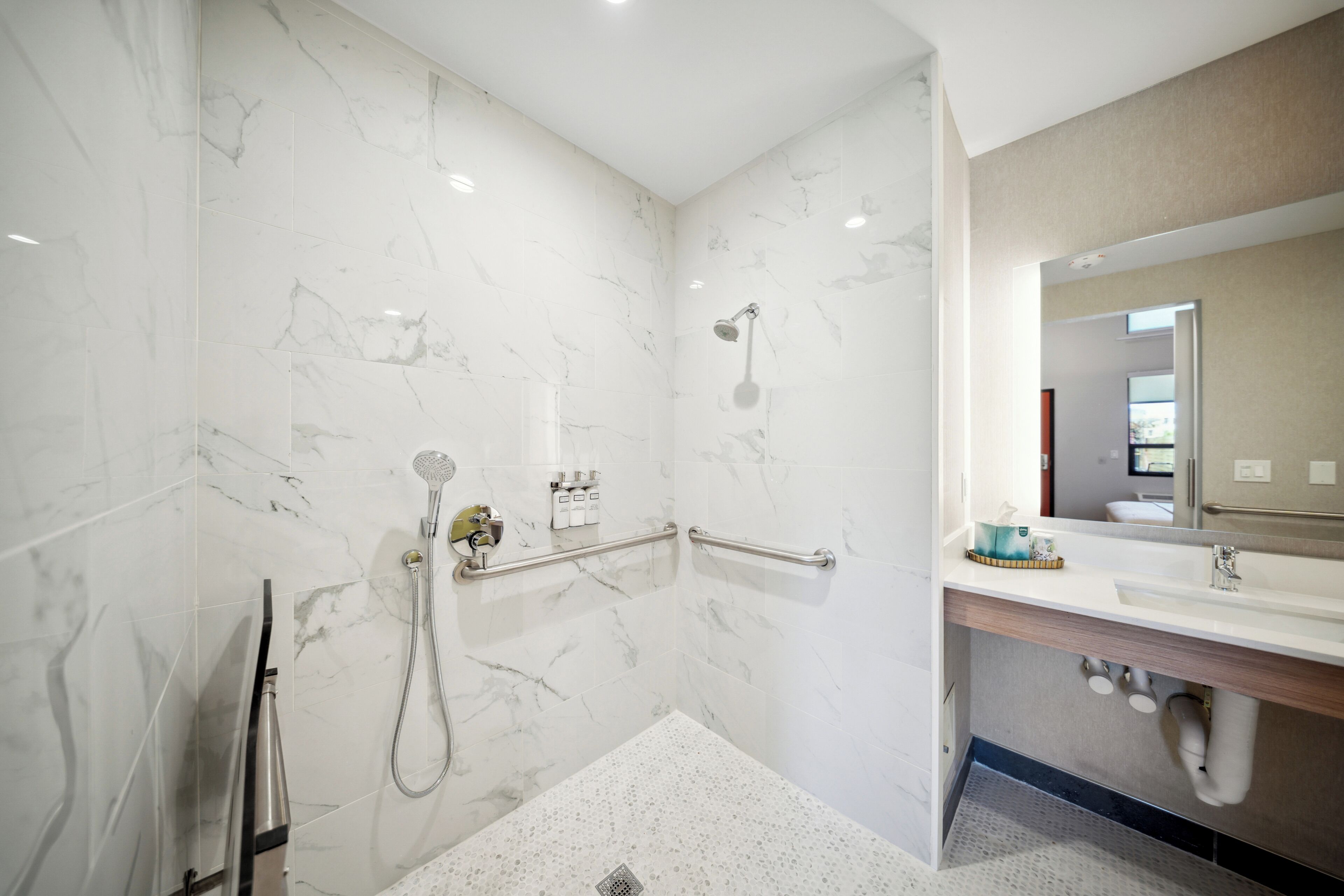 Un bagno moderno con pareti in marmo, una doccia con soffione manuale, un lavabo e uno specchio.