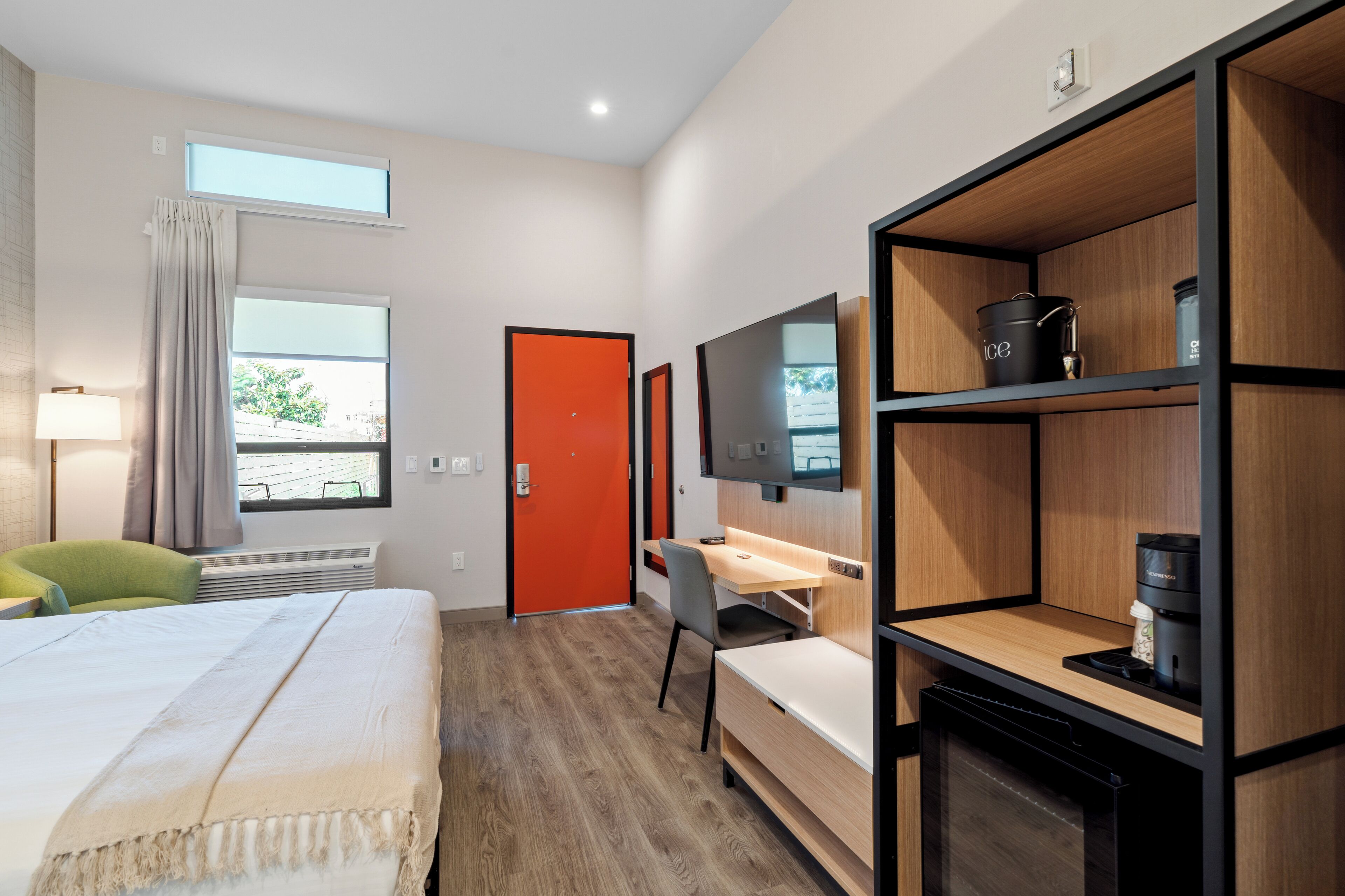 Una habitación de hotel moderna con cama, escritorio, silla, televisor y cafetera.