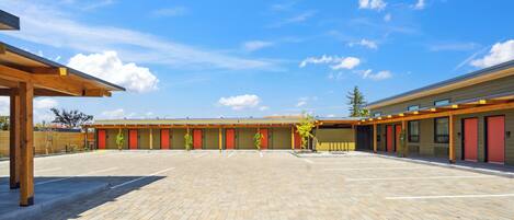 A building with a covered parking area and multiple rooms with red doors.