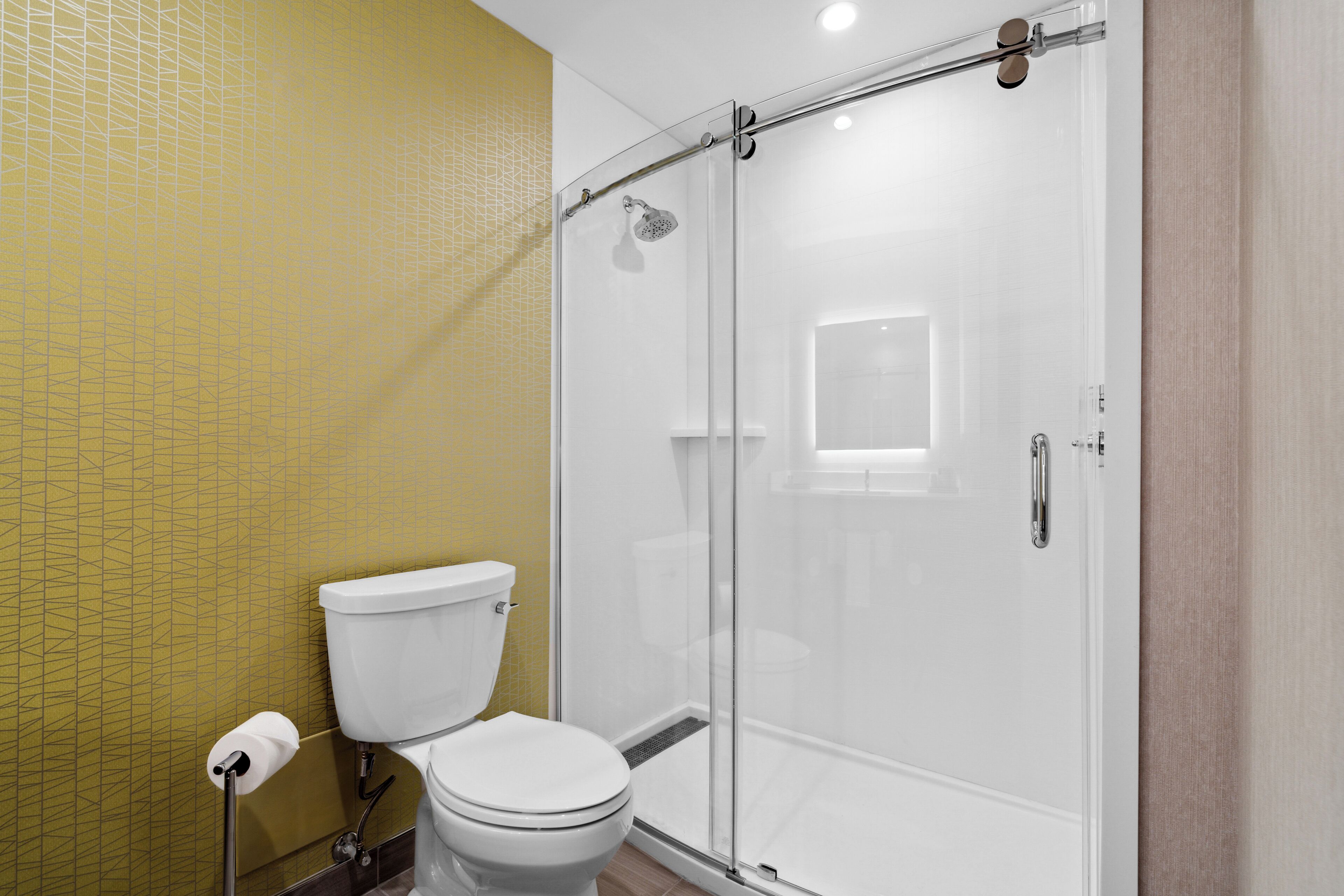 A bathroom with a toilet, a glass-enclosed shower, and a yellow patterned wall.